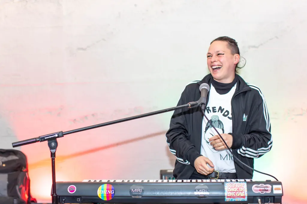 MIRI laughs at the microphone behind a sticker-covered keyboard.