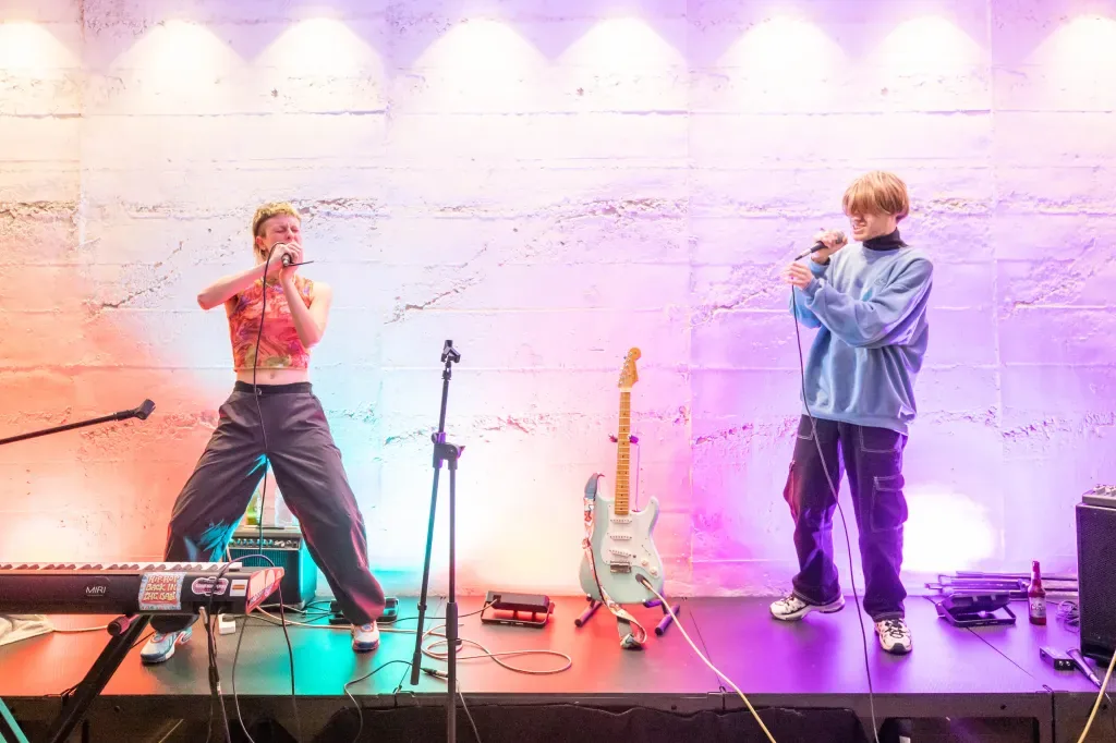 The two members of Try Me perform on a low stage washed in pink and violet light.